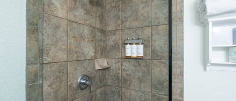 Eine Dusche mit Duschbrause, Wandarmatur und Ablage für Pflegeprodukte.