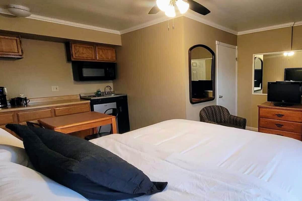 Ein Hotelzimmer mit einem Bett, einem Schreibtisch mit Computer, einem Sessel, einem Fernseher und einem Spiegel.