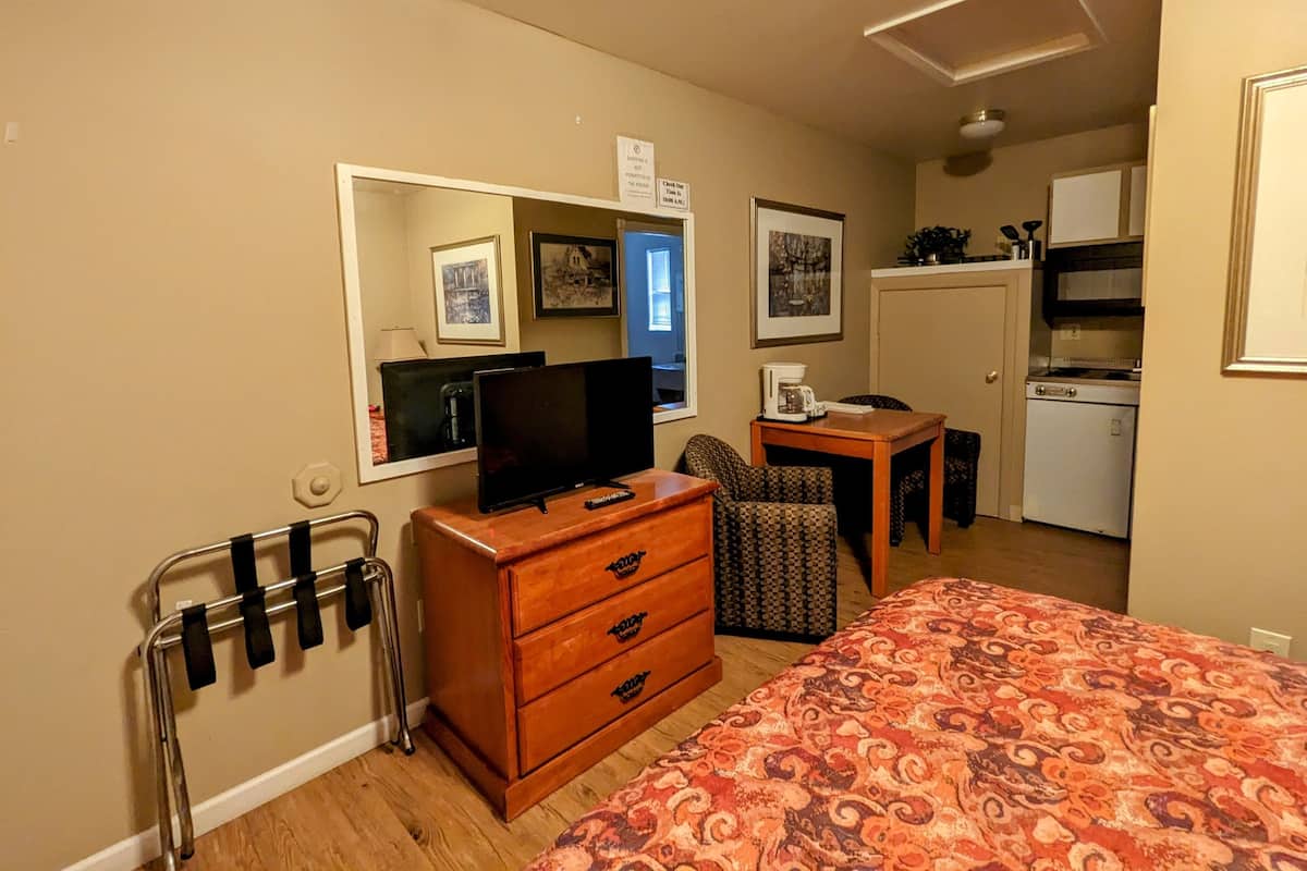 Ein kompaktes Hotelzimmer mit Bett, Schreibtisch, Stuhl, Fernseher, einer Küchenzeile und einem Badezimmer mit Dusche.