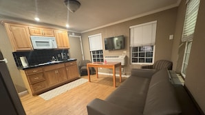 A compact living space with a kitchenette, a flat-screen TV mounted on the wall, a sofa, and a patterned armchair. - Bridge of The Gods (Cascade Locks)