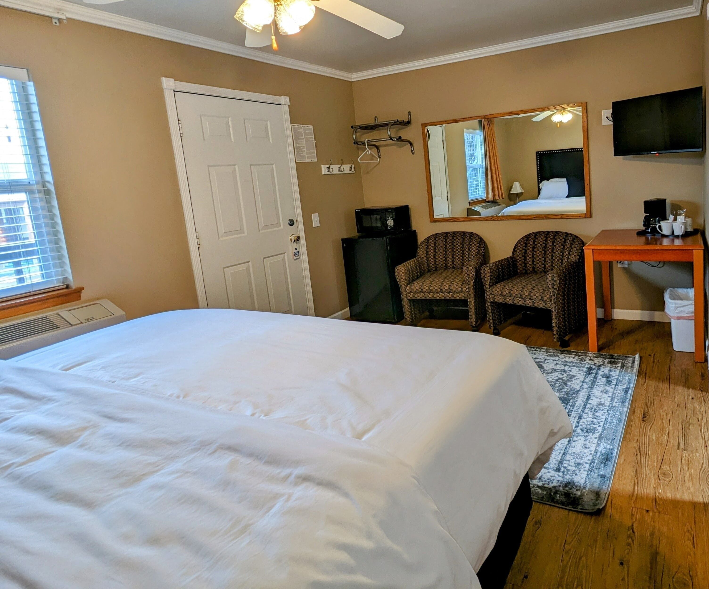 Een hotelkamer met een groot bed, twee gestreepe fauteuils, een bureau met een televisie en een plafondventilator.
