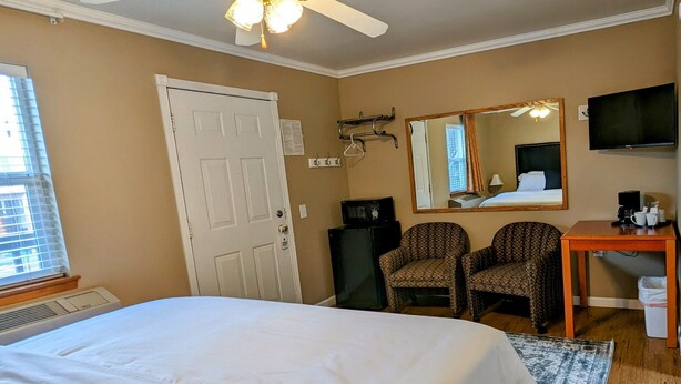 Quarto de hotel com uma cama grande, dois poltronas estampadas, uma escrivaninha com televisão e um ventilador de teto.