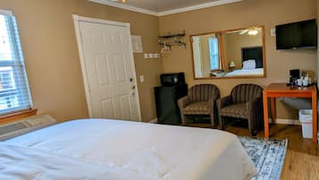 Een hotelkamer met een groot bed, twee gestreepe fauteuils, een bureau met een televisie en een plafondventilator.
