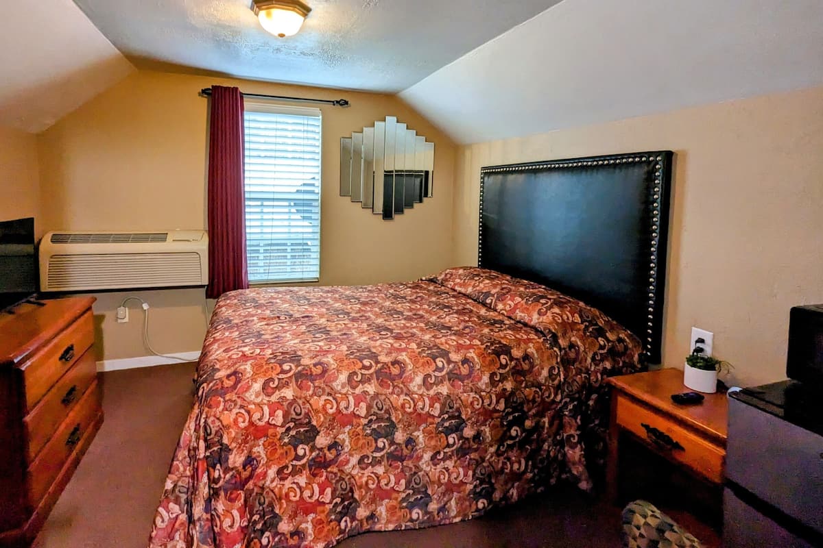 Ein Schlafzimmer mit einem Bett, einem Schminktisch, einer Klimaanlage, einem Fenster mit Jalousien und einer Deckenleuchte.