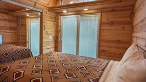 A wooden cabin bedroom with a bed, a ceiling fan, and large windows. - Bridge of The Gods (Cascade Locks)