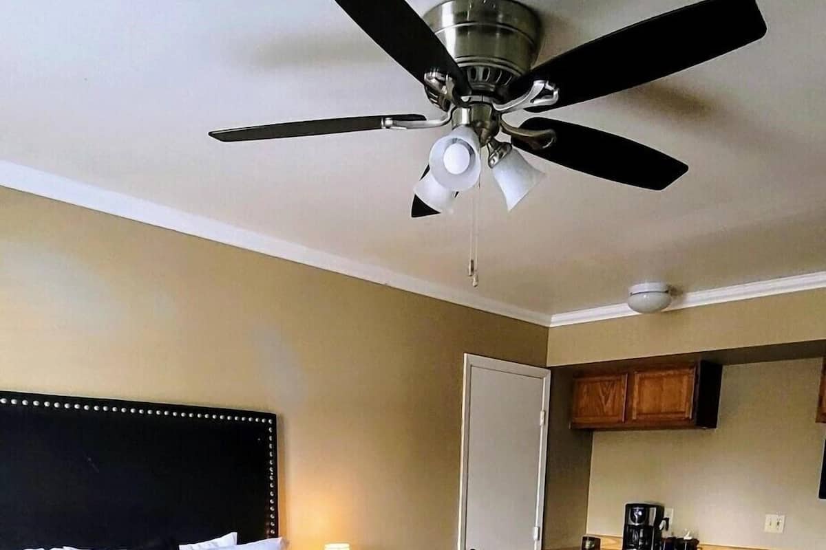 Ein Hotelzimmer mit Bett, Schreibtisch, Stuhl, Deckenventilator und einer Küchenzeile.