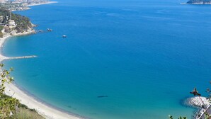 A coastal view with a clear blue sea, a sandy beach, and a rocky outcrop with a flag. - Gorgeous apartment in Alassio with WiFi (Alassio)