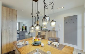 Enjoy meals in this dining area with a wooden table, pendant lights, and a fully equipped kitchen.