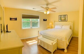 A bedroom with a bed, a ceiling fan, a window, and a bedside table.