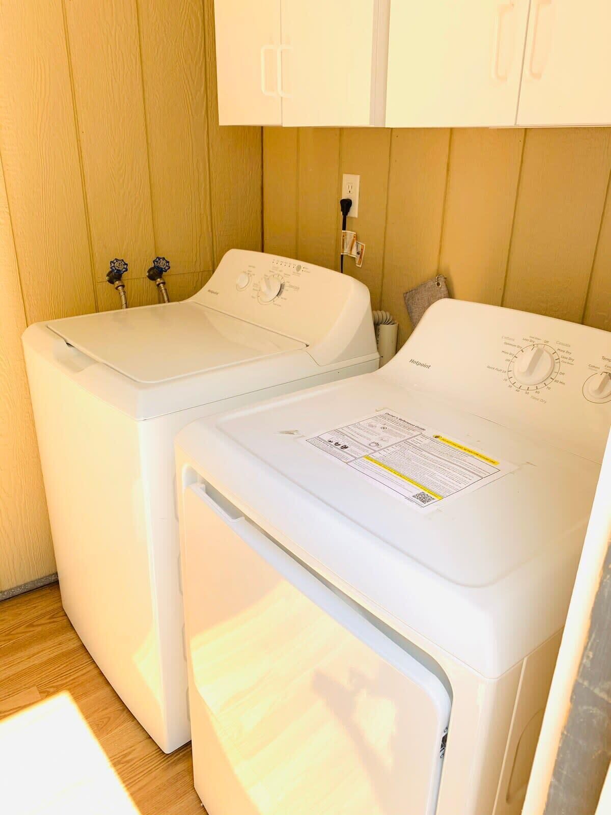 A laundry area with two white washing machines and a dryer, wooden panel walls, and a white cabinet above.