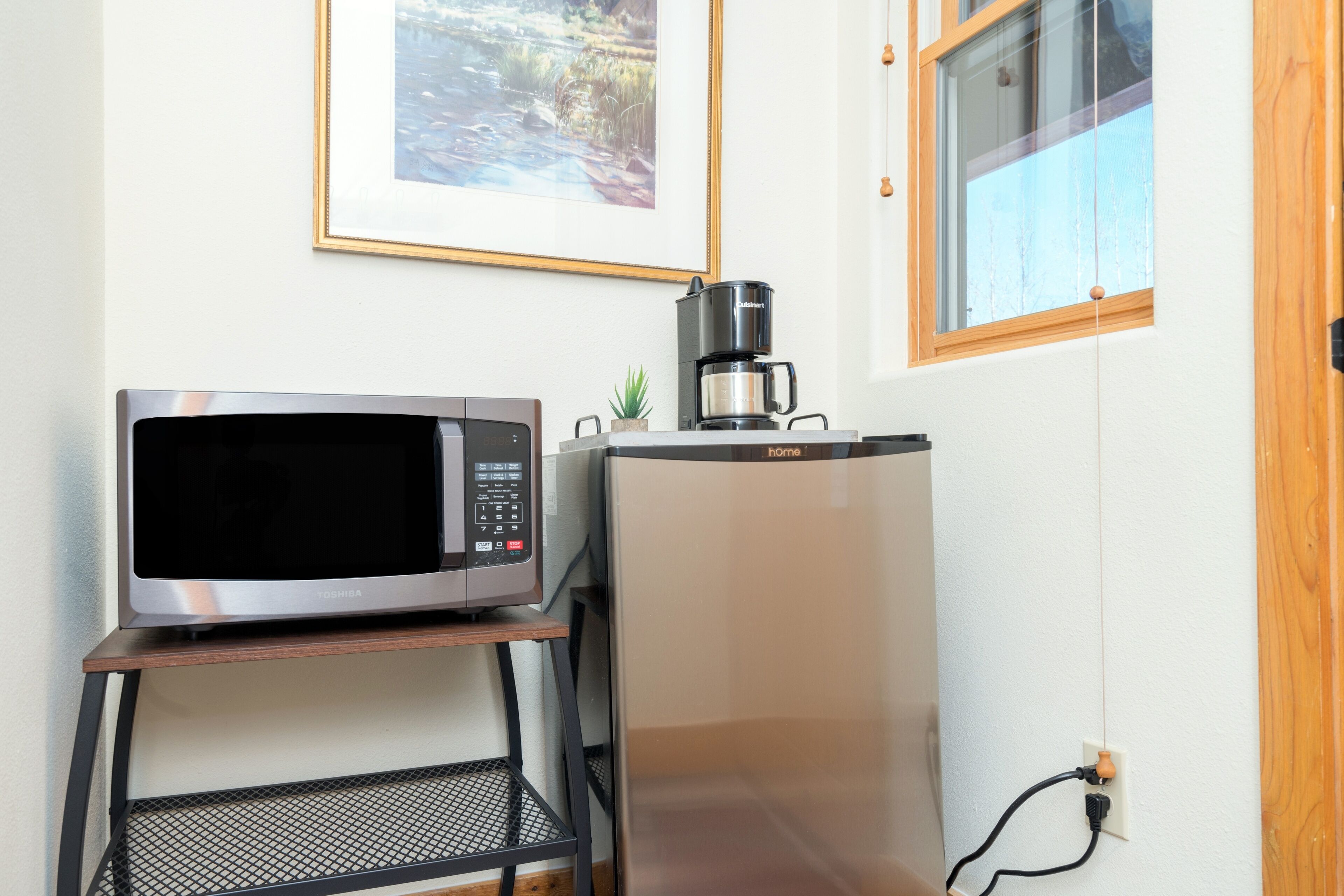 Una cocina con un microondas en un estante, una cafetera y un cuadro en la pared.