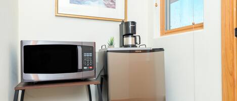 Una cocina con un microondas en un estante, una cafetera y un cuadro en la pared.