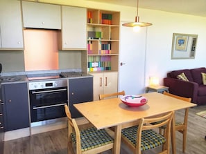 A compact kitchen with a built-in oven, a dining table with chairs, and a bookshelf with colorful books. - 2bed-beachfront Sea-view-norfolk Home-pet Friendly (Norwich)