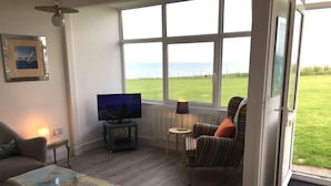 A living room with a television, a sofa, a striped armchair, a small table, and a colorful rug. - 2bed-beachfront Sea-view-norfolk Home-pet Friendly (Norwich)