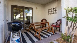 A covered patio with a barbecue grill, wooden table, and chairs.