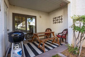 A covered patio with a barbecue grill, wooden table, and chairs. - Las Palmas Resort #1408 | All-Inclusive Amenities (Saint George)