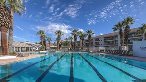 A swimming pool with clear water, surrounded by palm trees and a building with balconies.