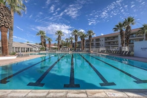 A swimming pool with clear water, surrounded by palm trees and a building with balconies. - Las Palmas Resort #1408 | All-Inclusive Amenities (Saint George)