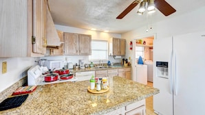 A kitchen with granite countertops, wooden cabinets, a ceiling fan, and a refrigerator. - Corpus Christi Extended Stay - 7 Mi to Beach! (Corpus Christi)