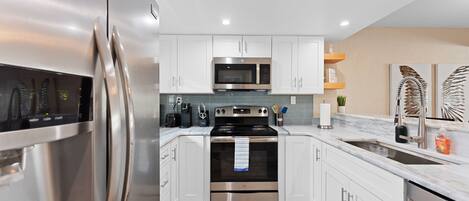 A modern kitchen with stainless steel appliances, white cabinetry, and a marble countertop.