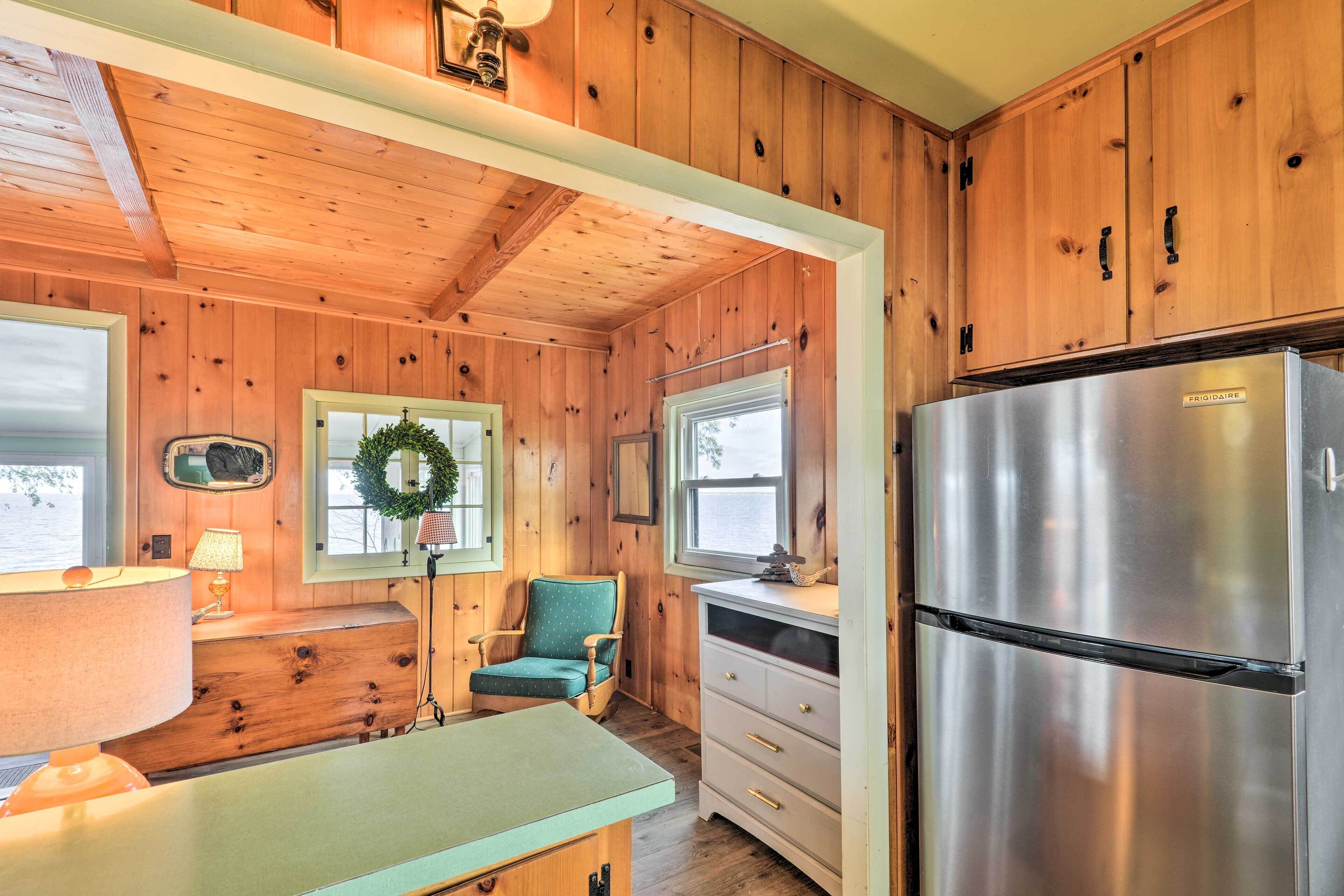 A wooden cabin interior with a kitchen area featuring a stainless steel refrigerator, a wooden dining table, and a green upholstered chair.