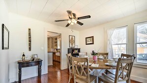 A dining area with a wooden table, chairs, and a ceiling fan. There is a kitchen in the background with cabinets and a countertop. - Charming Home Near Downtown Fredericksburg! (Fredericksburg)
