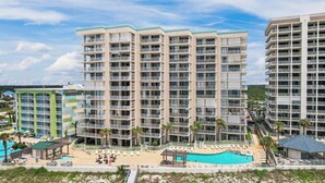 A multi-story hotel with balconies, a swimming pool, and a beach view.