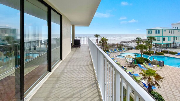A balcony with a view of the ocean and a pool area with lounge chairs.