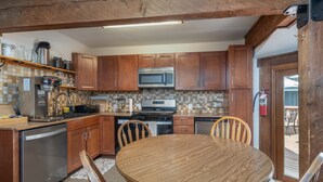 A kitchen with wooden cabinets, a stainless steel dishwasher, a microwave, and a wooden dining table with chairs. - Manitou Lodge 3 Hotel Room by Alpine Lodging Telluride (Telluride)