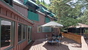 A wooden deck with outdoor furniture, a covered patio area, and a building with large windows and balconies. - Manitou Lodge 3 Hotel Room by Alpine Lodging Telluride (Telluride)