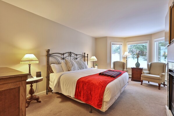 A bedroom with a bed, bedside lamps, a chair, a dresser, and a window with a view of trees. - The Birch Ridge: American Classic Room #7 - King Suite In Killington. Hot Tub. 1 Bedroom Home (Killington)
