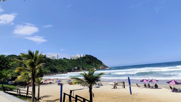Uma praia com palmeiras, guarda-sóis e uma rede de voleibol.
