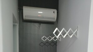 Un pasillo con una unidad de aire acondicionado vertical montada en una pared de metal corrugado, un estante metálico a la derecha y una puerta blanca a la izquierda.