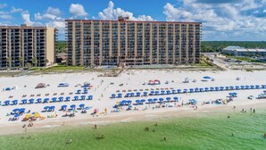 Un hôtel en bord de mer composé de plusieurs immeubles de grande hauteur, une plage de sable fin parsemée de nombreux parasols et un ciel bleu azur.