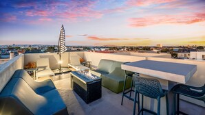 Una terraza en la azotea con una chimenea, zona de estar y vistas a la ciudad al atardecer.