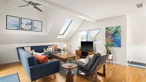 Una sala de estar moderna con sofá, sillón, mesa de centro, televisor y obras de arte.