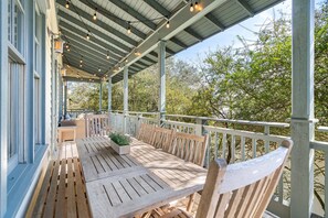 Een overdekt terras met een houten tafel en stoelen, een plantenbak en een balustrade.