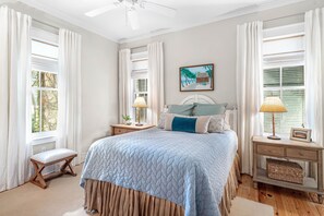 Een slaapkamer met een groot bed, twee nachtkastjes, een bankje en een plafondventilator.