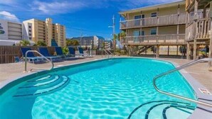 Una piscina con acqua cristallina e blu, circondata da sdraio e un edificio con balconi.