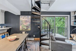 Ein modernes Interieur mit einer Wendeltreppe, einem Essbereich und einem Balkon mit Blick auf Grünflächen.