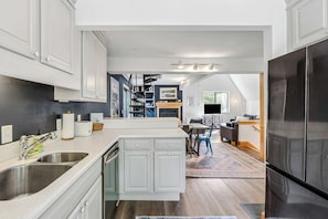 A modern kitchen with white cabinets, stainless steel appliances, and a dining area with a table and chairs. - Quechee Club Pool & Golf | 4BR Kingswood 10A (Quechee)
