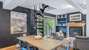 Un interior moderno con comedor, escalera de caracol, chimenea y obras de arte en las paredes.