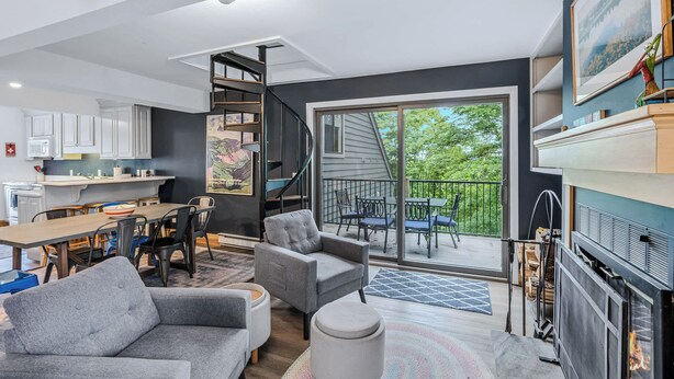 Un espacio habitable moderno con comedor, sofá, chimenea y un balcón con vistas a árboles.