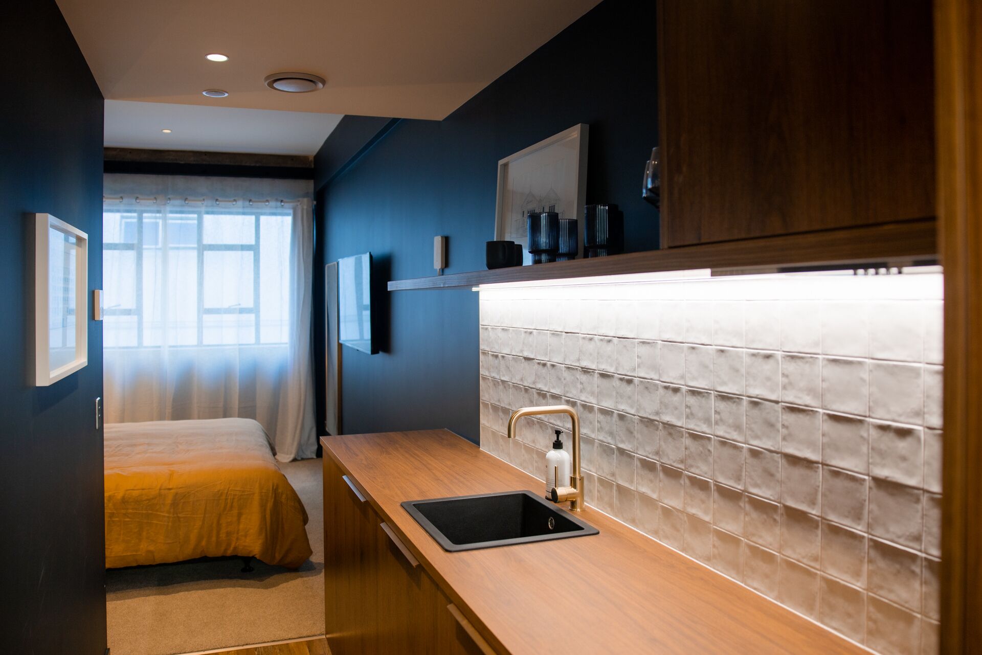 Une chambre d’hôtel de taille réduite, comprenant un lit, une petite kitchenette et une grande fenêtre.