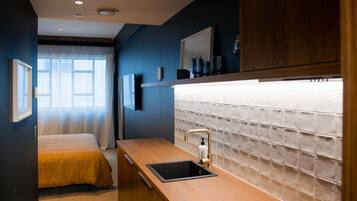 Une chambre d’hôtel de taille réduite, comprenant un lit, une petite kitchenette et une grande fenêtre.