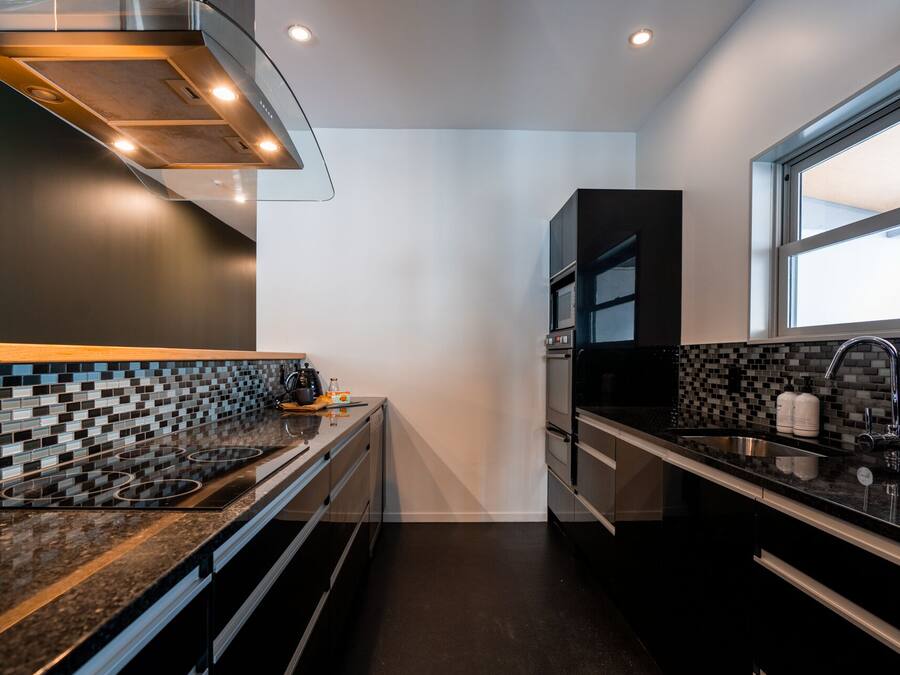 A modern kitchen with a black and white tiled backsplash, stainless steel appliances, and a window providing natural light.