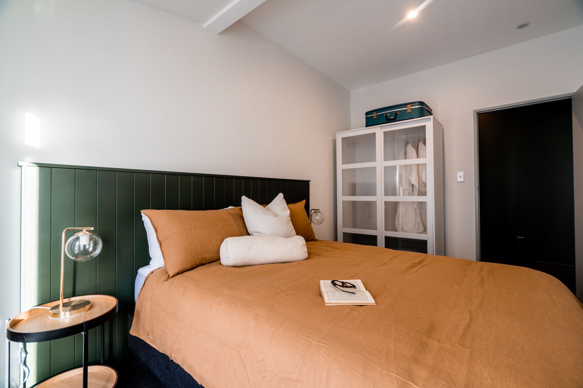 A neatly made bed with a brown cover, a bedside table with a lamp, and a wardrobe with a mirror.