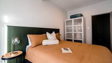 A neatly made bed with a brown cover, a bedside table with a lamp, and a wardrobe with a mirror.