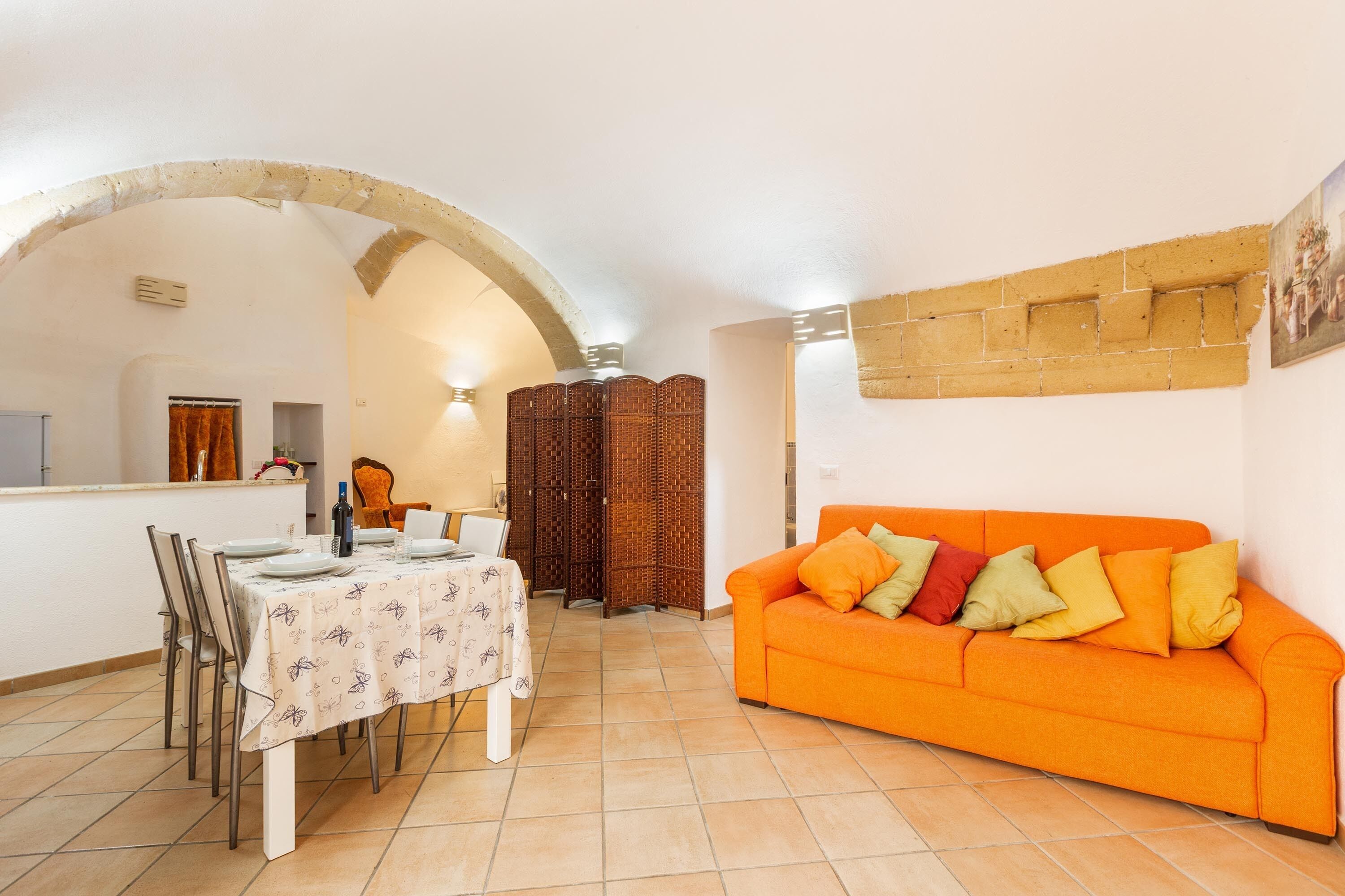 A dining area with a table set for four, a sofa with cushions, and a decorative partition.