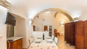 A dining area with a table set for four, a television mounted on the wall, and a brick archway leading to another room. - 3180 Appartamento Raffaella by Barbarhouse (Gallipoli)
